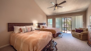 A bedroom with two beds, a ceiling fan, a sofa, and a view of the outdoors through large windows. - The Iron Cactus on the Comal CW C102 2 Bedroom Condo by RedAwning (New Braunfels)