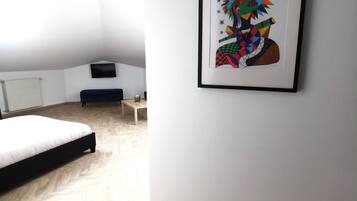 Habitació moderna amb un paviment de fusta en rel d'ós, un llit, una taula petita i un quadre abstracte amb marc a la paret.