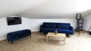 Un saló modern amb un sofà blau, un otomà a joc, una taula de centre de fusta i una làmpada de peu.