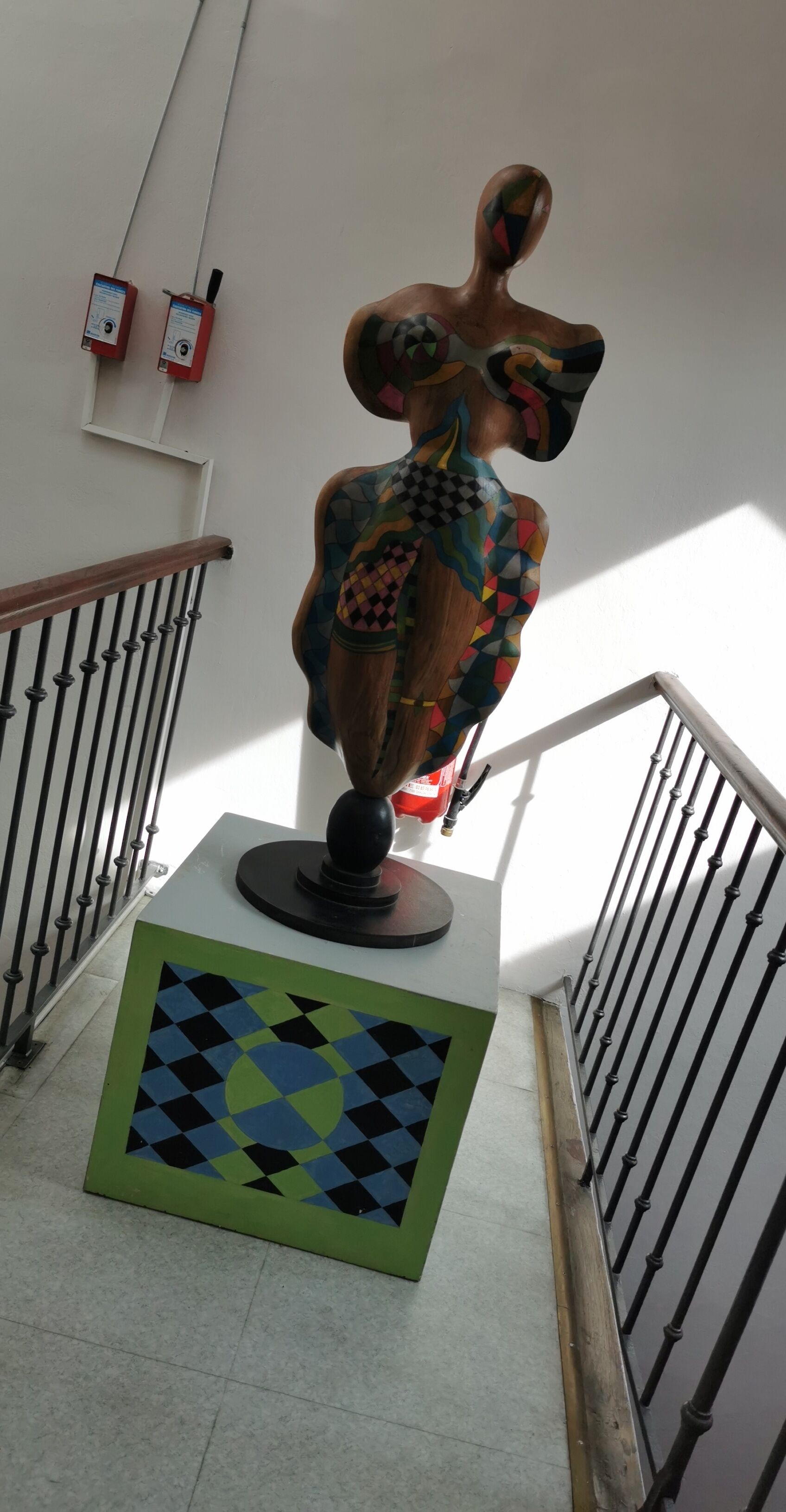 Una scala con una scultura decorativa, un tappeto a motivi e due dispositivi fissati al muro.