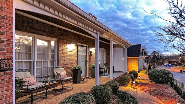 A brick house with a covered porch, outdoor seating, and well-lit landscaping.