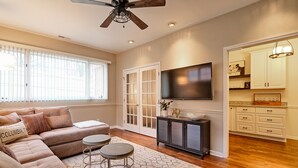 A living room with a sofa, two round tables, a TV, and a ceiling fan.