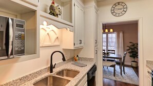 A kitchen with granite countertops, a double sink, a microwave, and a clock on the wall.