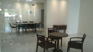 A modern dining area with a glass partition, wooden tables and chairs, and a tiled floor. - Hotel Recanto Vip (Araripina)
