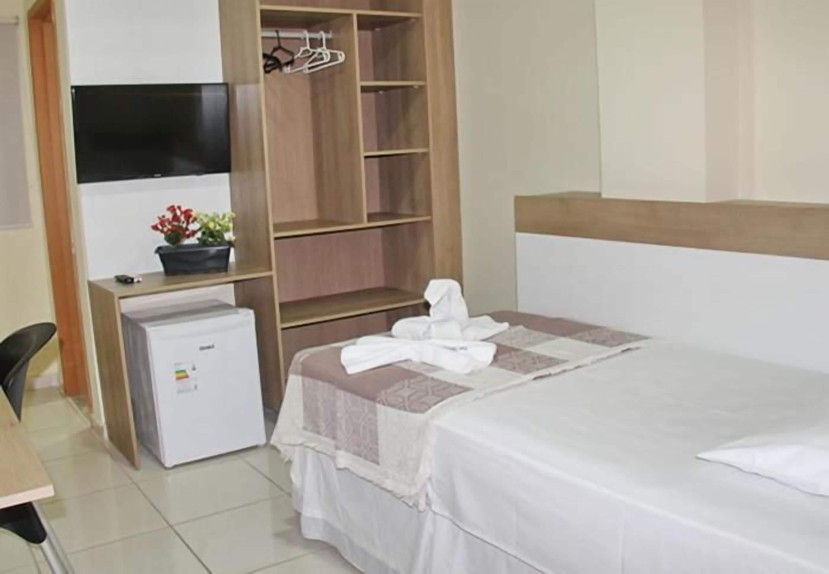 Habitació d'hotel amb llit, escriptori, armari i nevera petita.