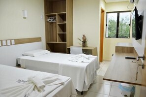 A hotel room with two beds, a wooden wardrobe, a small table with a vase, and a window with a view of greenery. - Hotel Recanto Vip (Araripina)