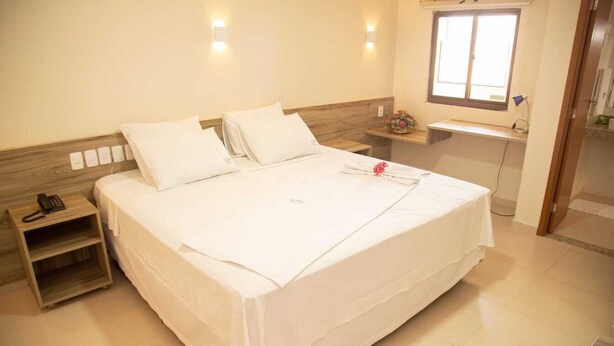 A hotel room with a large bed, bedside tables, a desk, and a window. - Hotel Recanto Vip (Araripina)