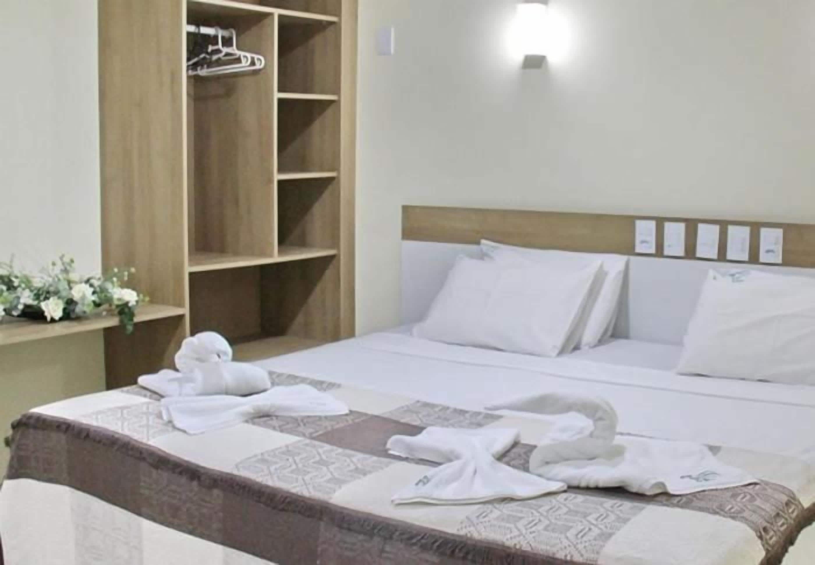 Une chambre d’hôtel avec un lit, une armoire en bois et un luminaire fixé au mur.