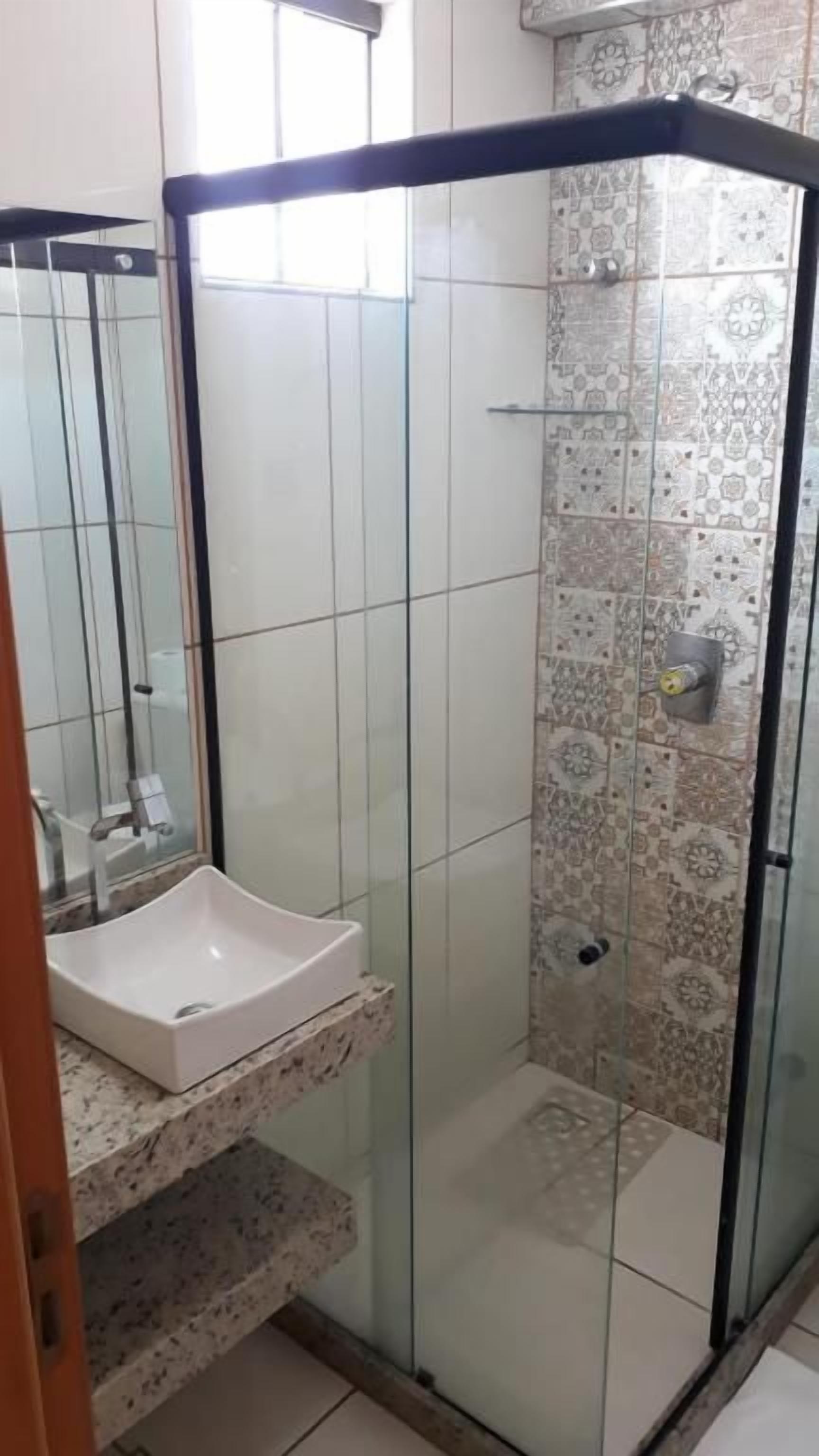 A bathroom with a glass-enclosed shower, a white sink, and patterned tiles.