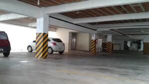 A parking garage with concrete pillars, a white car, and a red car. - Hotel Recanto Vip (Araripina)