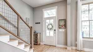 A staircase with wooden steps and a metal railing, a white door with a glass panel, and a wall-mounted light switch.