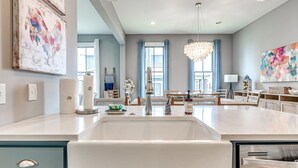 A modern kitchen with a large island, a dining area with a chandelier, and artwork on the walls.