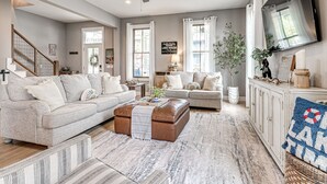 A spacious living room with a grey sofa, a brown ottoman, and a striped rug.