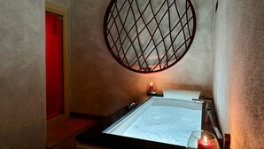 A bathroom with a bathtub, a round mirror, and a red door.