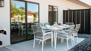 An outdoor patio with a white table and chairs, a glass door leading to a garden, and a black fence. - V 31| 3-Level Townhome *Pool* Hot Tub * Pickleball (St. George)