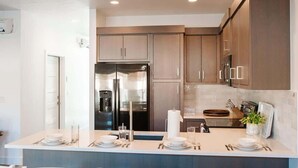 A modern kitchen with dark wooden cabinets, stainless steel appliances, and a central island with a sink and dining area. - V 31| 3-Level Townhome *Pool* Hot Tub * Pickleball (St. George)
