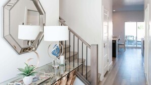 A modern interior with a glass console table, a hexagonal mirror, and a staircase leading to a balcony. - V 31| 3-Level Townhome *Pool* Hot Tub * Pickleball (St. George)