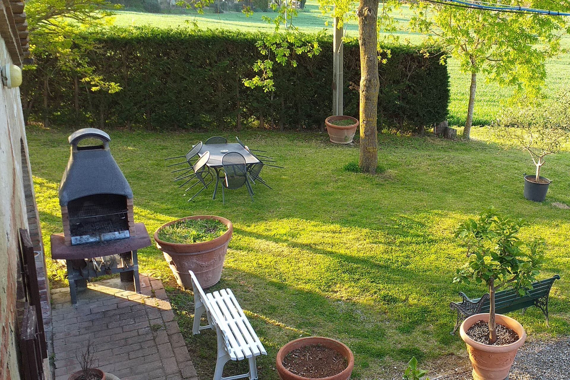 A backyard with a barbecue grill, a table with chairs, and several potted plants.