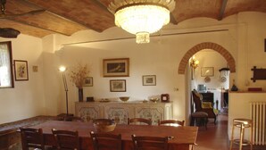 A dining area with a large wooden table, chairs, and a chandelier. There are framed pictures on the walls and a radiator in the background. - Casalunga, beautiful farmhouse with swimming pool and garden (Buonconvento)