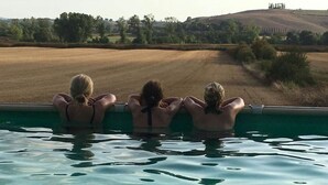Three individuals relaxing by a pool with a view of a field and hills in the background. - Casalunga, beautiful farmhouse with swimming pool and garden (Buonconvento)