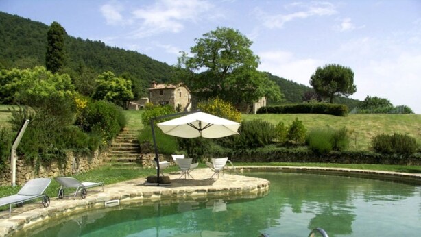 A pool area with lounge chairs and an umbrella, surrounded by lush greenery and a stone building in the background. - Case Belle, beautiful villa in the heart of the Val d'Orcia with 12 sleeping accommodations (Sarteano)