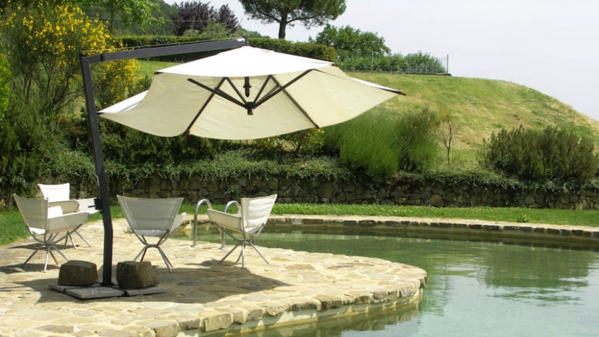 A poolside area with a stone deck, two white lounge chairs, and a large umbrella.