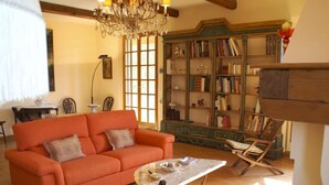 En hyggelig stue med en stor orange sofa, et glasbord og en reol fyldt med bøger og pynteting.