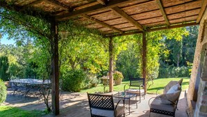 An outdoor patio with wooden tables and chairs, surrounded by lush greenery and a wooden pergola. - Villa La Felce, a typical Tuscan farmhouse surrounded by nature (Cetona)