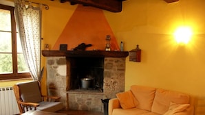 A cozy living room with a stone fireplace, a wooden chair, and a sofa. - Splendid villa with view in Castiglioncello sul Trinoro (Castiglioncello sul Trinoro - Sarte)