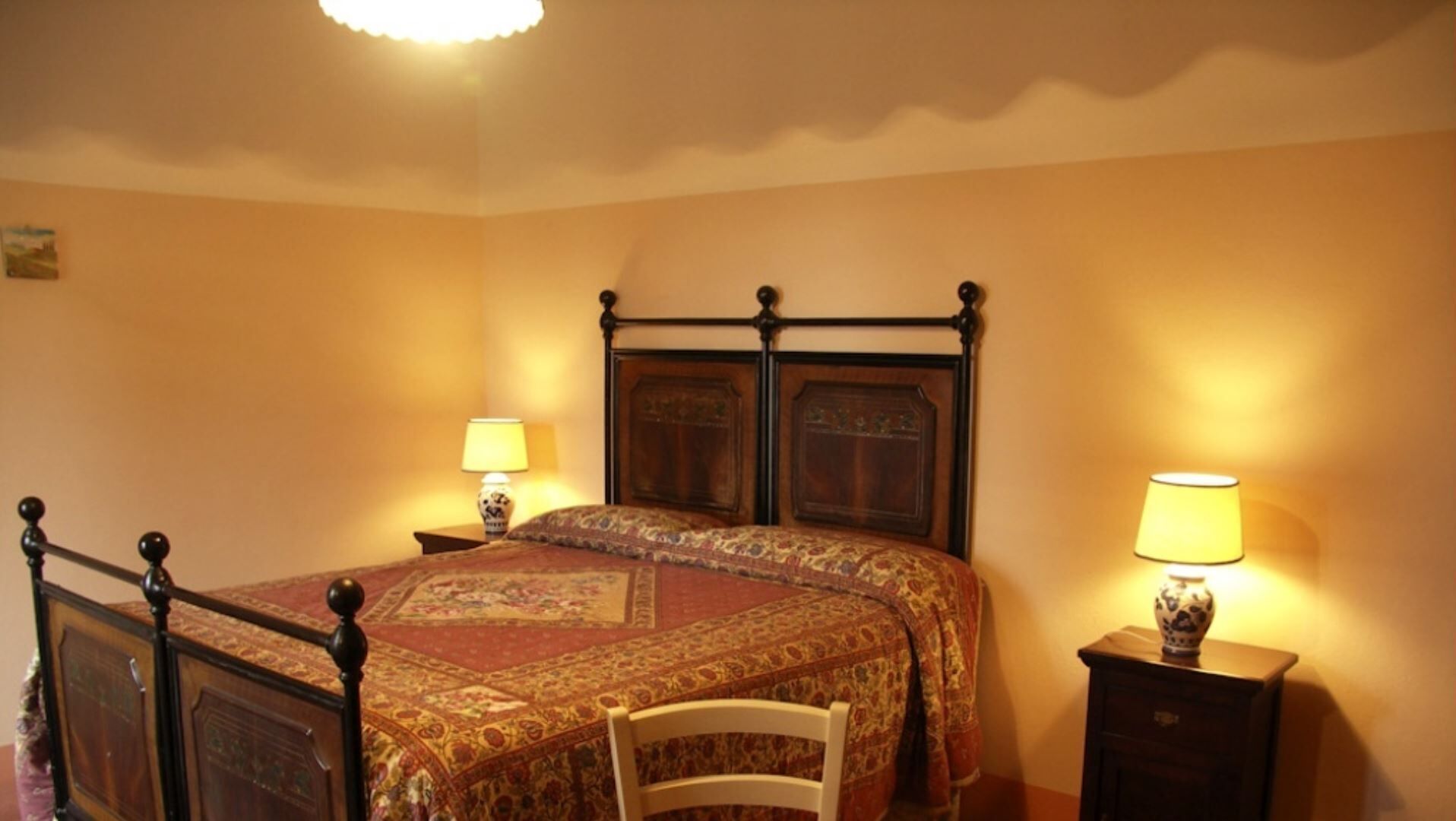 A bedroom with a four-poster bed, two bedside tables with lamps, and a chair.