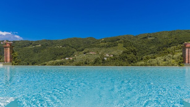 A clear blue pool with a view of a green hillside and a brick structure. - Villa Roncosi, beautiful 15-bed villa with jacuzzi (Monsummano Terme)
