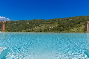 Una piscina azul cristalina con vistas a una ladera verde y una construcción de ladrillo.