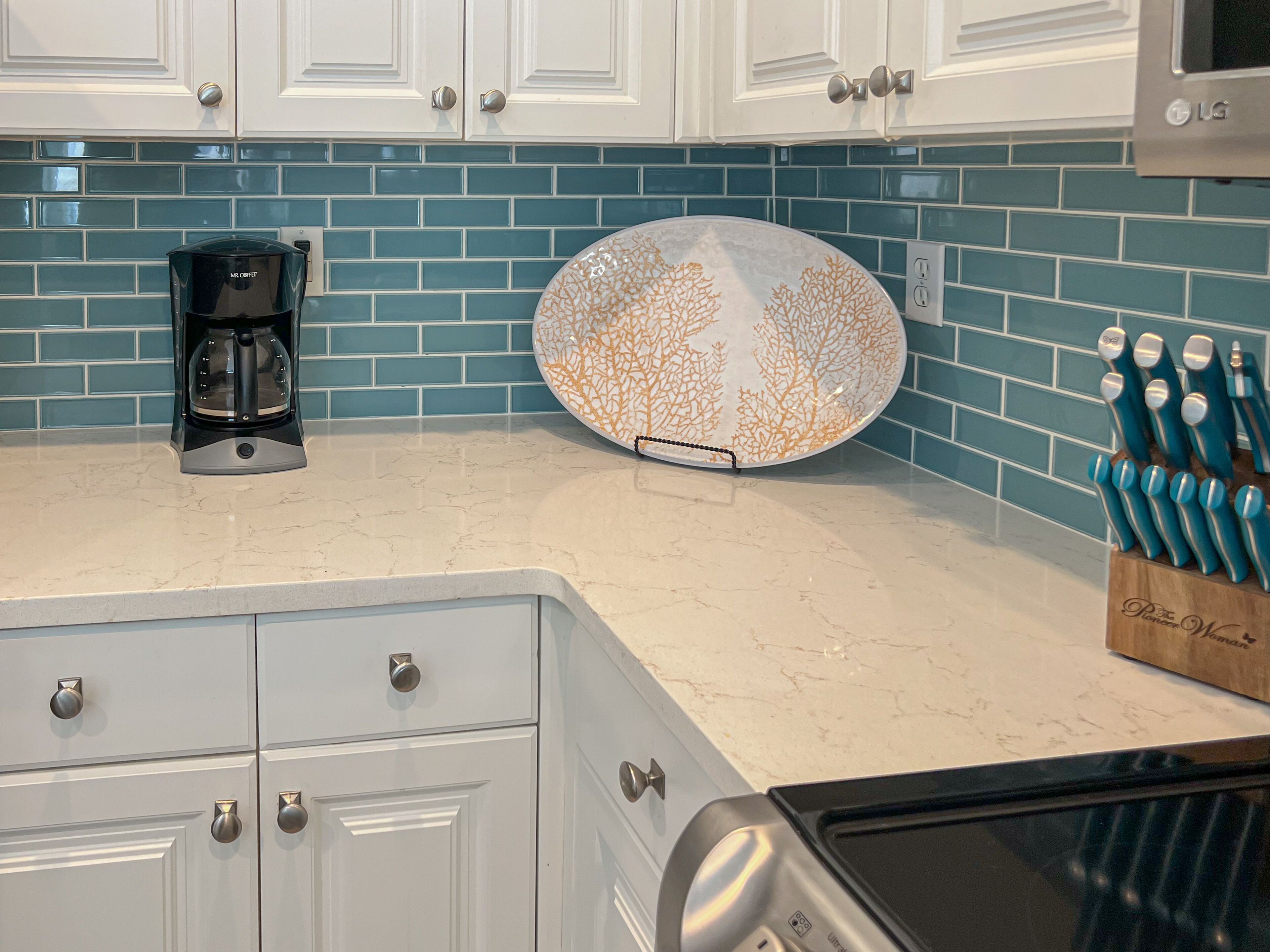 A kitchen with white cabinets, a coffee maker, a decorative plate, and a knife block.