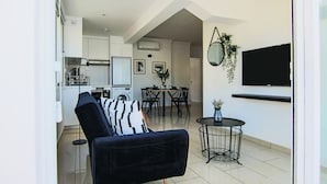 Eine moderne Wohnung mit einem schwarzen Sofa, einem Essbereich, einer Küche und einem an der Wand befestigten Fernseher.