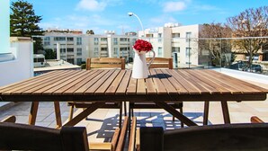 Ein Holztisch mit Stühlen und einer weißen Vase mit roten Blumen auf einer Dachterrasse.