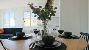 Ein Esstisch, gedeckt mit schwarzen Schalen, Weingläsern und einer Vase mit grünen Blättern.