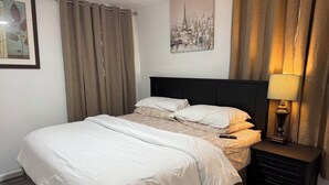 Una cama bien hecha con una colcha estampada, una lámpara de noche y un cuadro colgado en la pared.