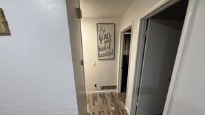 Un pasillo con piso de madera, pared blanca y un cartel con una frase motivacional.