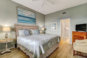 Un dormitorio con una cama grande, televisor, cómoda y un cuadro en la pared.