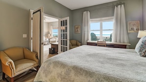 A bedroom with a large bed, a chair, a desk, a window with curtains, and a view of the outdoors. - Gorgeous Ocean Views | Ocean Park Penthouse | Garage Access | Easy Walk to Beach (Fernandina Beach)