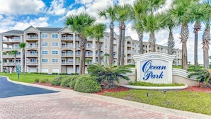 A multi-story hotel with a sign reading "Ocean Park" and a paved walkway with palm trees. - Gorgeous Ocean Views | Ocean Park Penthouse | Garage Access | Easy Walk to Beach (Fernandina Beach)