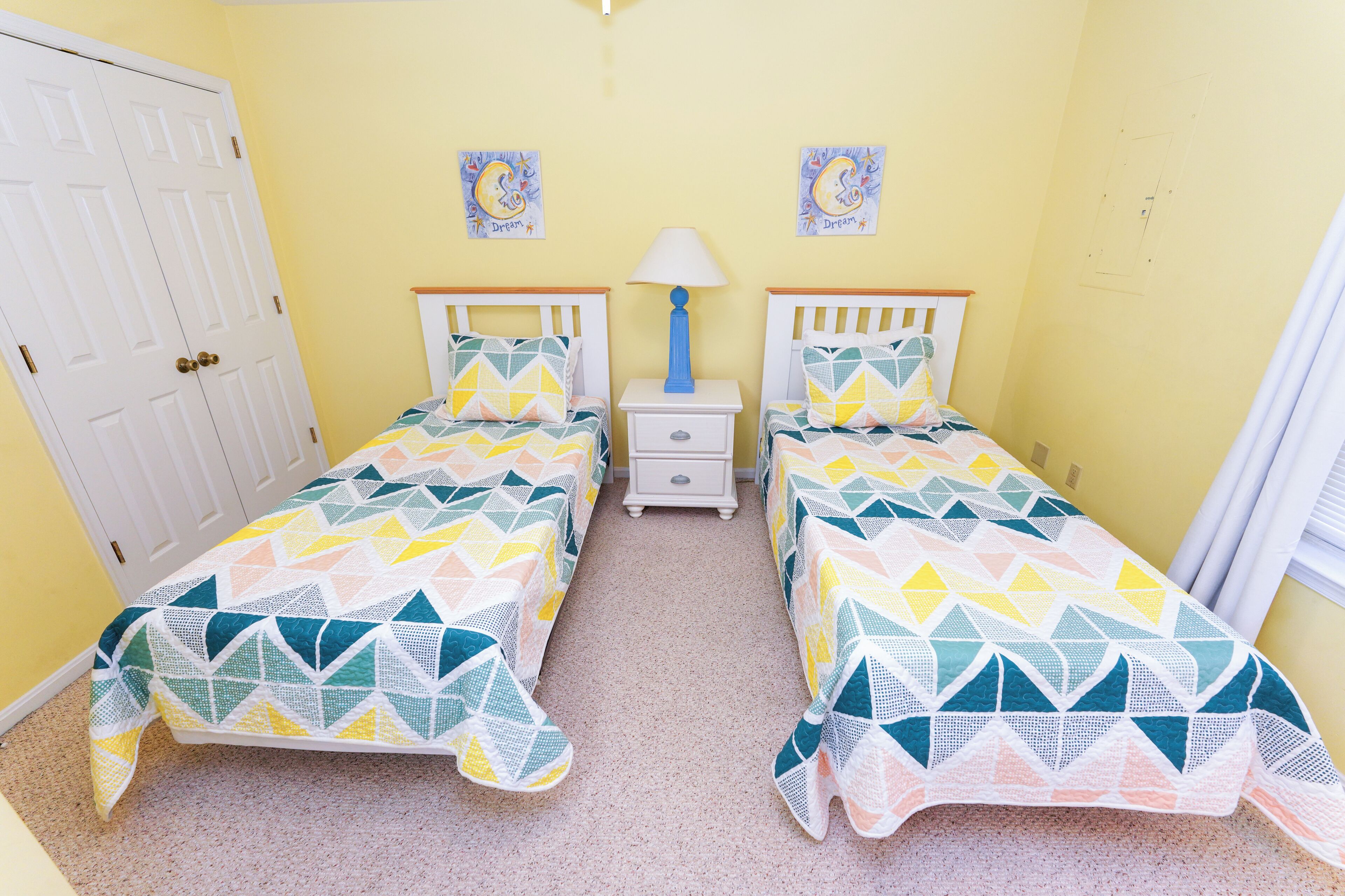 A room with two beds, a nightstand, a lamp, and a door.