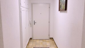 Un couloir avec une porte blanche, un petit tapis sur le sol et un tableau encadré au mur.