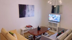 Un salon moderne avec un canapé, une table basse, un téléviseur posé sur un meuble et des œuvres d’art abstraites accrochées au mur.