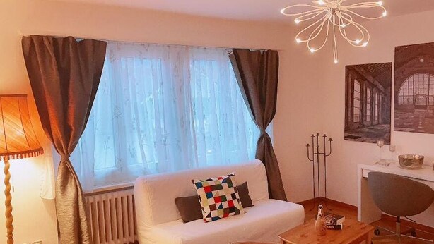 Un salon chaleureux avec un canapé blanc, une table basse et une cheminée. Trois tableaux encadrés ornent le mur, et une lampe se trouve à gauche.