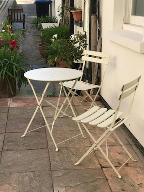 Uma mesa dobrável de metal branco e duas cadeiras de metal branco num pátio de pedra.