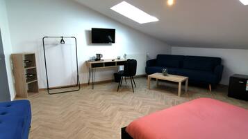 Una habitación moderna y bien iluminada con una cama estilo altillo, un escritorio con computadora, un televisor y un sofá.