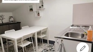 Une cuisine avec une table et des chaises blanches, un évier et une cuisinière. Il y a trois petites étagères au mur.