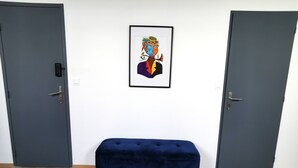Une pièce avec deux portes grises fermées, un banc en velours bleu et un tableau abstrait encadré accroché au mur.