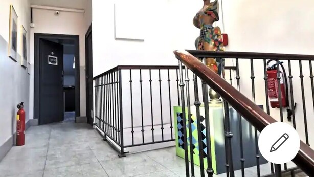 Un couloir avec un extincteur, une porte fermée et une statue sur un piédestal.